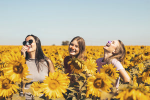 Couple of girls playing in a field of sunflowers wearing Nöz nose sunscreen